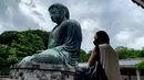 Seorang perempuan bermasker mengunjungi The Great Buddha atau yang biasa disebut Kamakura Daibutsu di kuil Kotoku-in di Kamakura, Prefektur Kanagawa, Jepang, Sabtu (20/6/2020). Patung Buddha dari perunggu yang menjulang dengan tinggi 13,35 meter ini didirikan tahun 1252. (Behrouz MEHRI/AFP)