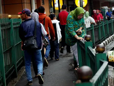 Seorang ibu berusaha melompati pagar pembatas di Stasiun Cikini, Jakarta Pusat, Rabu, (20/12). Akses pintu keluar stasiun yang terlalu jauh membuat banyak penumpang yang mencari jalan pintas dengan melompat pagar. (Liputan6.com/Johan Tallo)