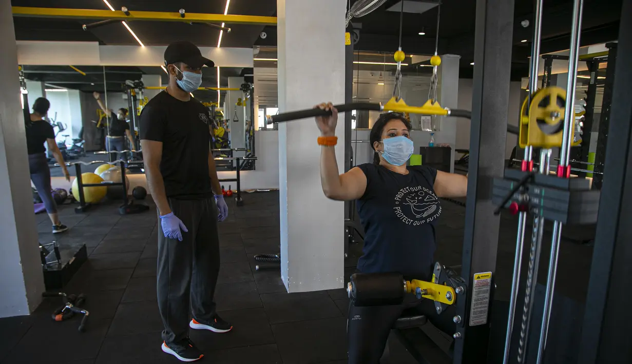 Seorang pelatih terlihat ketika seorang wanita India berolahraga di sebuah gym yang dibuka kembali setelah dikurung di Gauhati, India, Rabu, (5/8/2020). India memiliki jumlah virus coronavirus tertinggi ketiga di dunia setelah Amerika Serikat dan Brasil. (AP Photo/Anupam Nath)