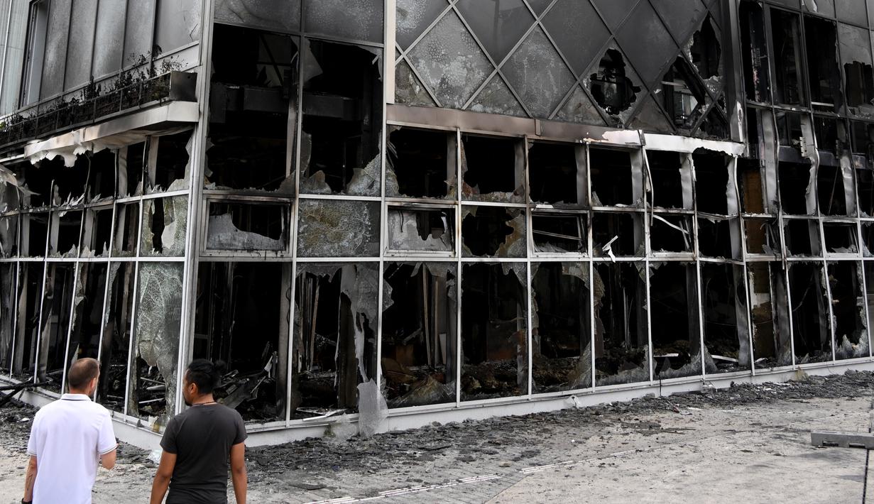 Dua pria melihat fasad Hotel du ville yang hangus dan terbakar di Garges-les-Gonesse, utara Paris, menyusul kerusuhan dua hari setelah seorang remaja 17 tahun ditembak di dada oleh polisi dari jarak dekat di Nanterre, pinggiran barat Paris, pada 29 Juni 2023. (Photo by Bertrand GUAY / AFP)