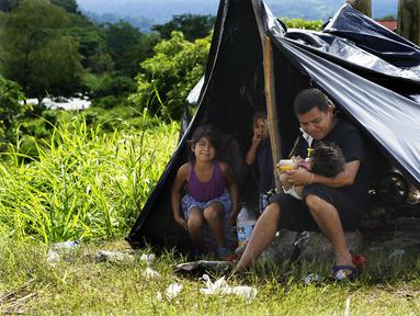 Seorang ayah memberi susu botol jus jeruk kepada putrinya yang masih bayi di tepi Sungai Huixtla, negara bagian Chiapas, Meksiko, Rabu (8/5/2022). Keluarga itu adalah rombongan dari kelompok migran, banyak dari Amerika Tengah dan Venezuela, yang meninggalkan Tapachula. (AP Photo/Marco Ugarte)