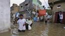 Warga melintasi jalan banjir setelah hujan deras di Karachi, Pakistan, Minggu, (26/7/2020). Sebagian warga memilih untuk bertahan meski rumah mereka terendam banjir. (AP Photo/Fareed Khan)