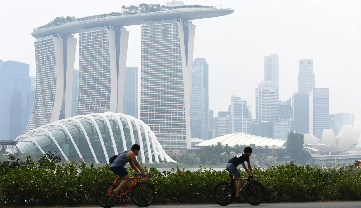 Dua pria mengendarai sepeda saat kabut asap menyelimuti kota Singapura (15/9/2019). Akibat kabut asap yang terjadi di kota tersebut membuat Grand Prix Formula 1 di Singapura pekan depan, 20-22 September 2019, terancam batal.  (AFP Photo/Roslan Rahman)