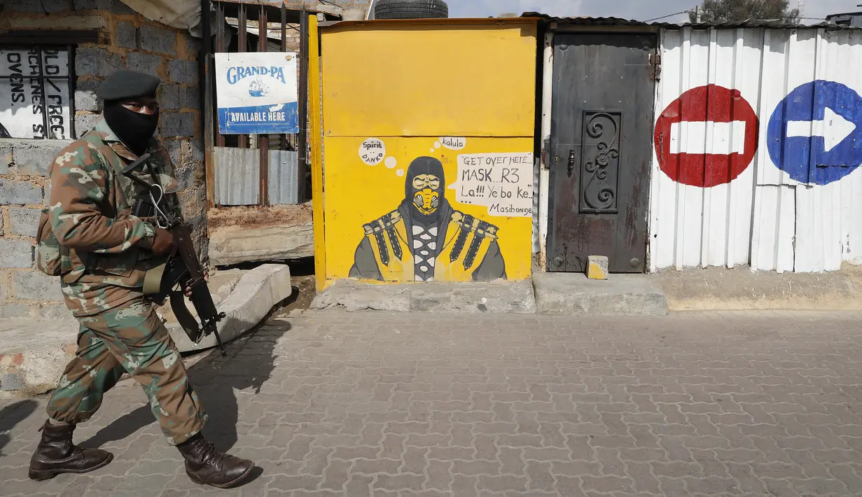 Seorang anggota Pasukan Pertahanan Afrika Selatan (SANDF) berjalan melewati mural yang mengiklankan penjualan masker saat berpatroli di di Alexandra, Johannesburg, Kamis (15/7/2021). Patroli tersebut menyusul kerusuhan massa yang disebabkan dipenjaranya mantan Presiden Jacob Zuma (Phill Magakoe/AFP)