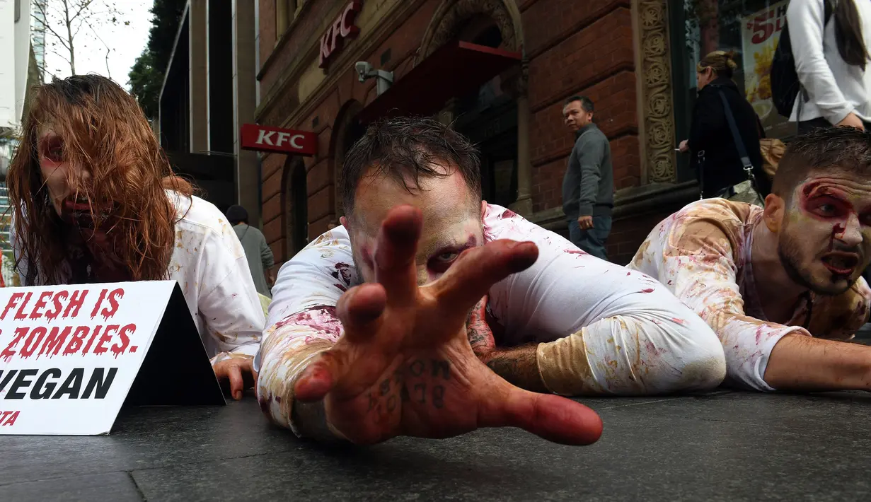 Pejalan kaki mengamati aktivis PETA yang berdandan menyerupai zombie sambil berbaring di jalan depan sebuah restoran cepat saji di Sydney, Kamis (15/6). Aksi itu sebagai bentuk protes terhadap konsumsi daging dan mempromosikan vegetarian (SAEED KHAN/AFP) 