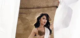 Cinta Laura tampil bak Dewi Athena dengan gaun putih berbahan chiffon yang dililitkan asimetris dan berpotongan cut-out di pinggang. Atasan berhias kristal emas serta bros bunga matahari dari batu kristal besar menjadi pusat perhatian, dipadukan sayap bulu emas yang megah dan heels gladiator emas bertali tinggi. [@claurakiehl]