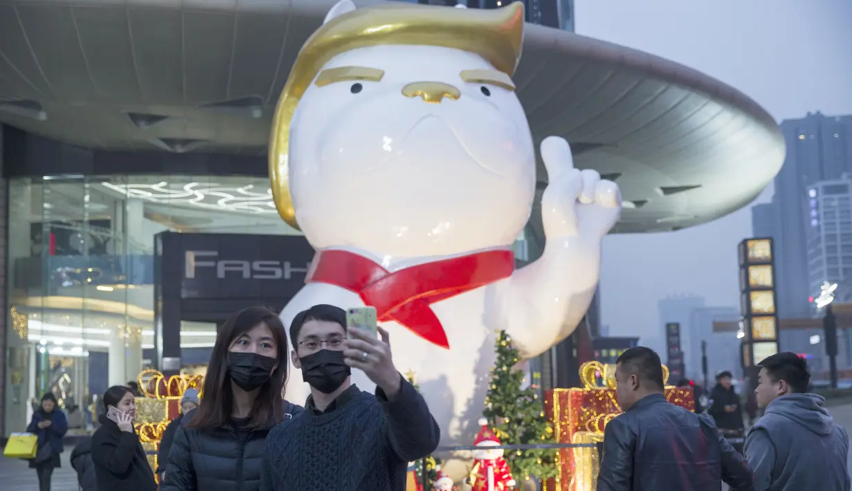 Sepasang pengunjung berswafoto dengan latar belakang patung anjing raksasa mirip Presiden AS Donald Trump di Festival Walk Mall, Shanxi, Tiongkok, Jumat (29/12). Keberadaan patung ini untuk menyambut datangnya tahun anjing tanah. (STR / AFP)