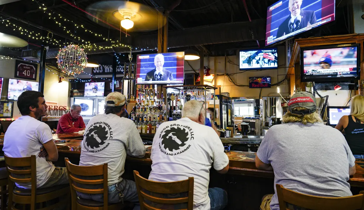 Sejumlah pria duduk di bar sementara Presiden Joe Biden menyampaikan pidato pelantikannya di televisi di belakang bar, di Ferg's Sports Bar di St. Petersburg, Florida (20/1/2021).  Joe Biden menjadi presiden AS tertua dalam sejarah. (Martha Asencio Rhine/Tampa Bay Times via AP)