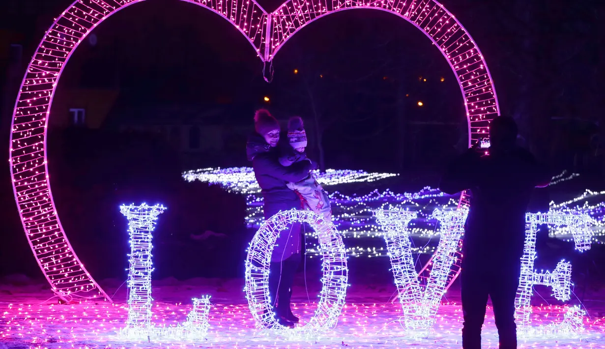 Seorang wanita bersama anaknya berfoto bersama diantara cahaya lampu yang memenuhi sebuah taman di Minsk, Belarus (5/2). Setelah matahari terbenam empat puluh pameran seni instalasi lampu menghiasi seluruh taman di Belarus. (AP Photo/Sergei Grits)