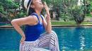 Saat liburan, Ayu Dewi memadukan tank top biru dengan colored stripe pants. Outfit santai ini tampak feminin dengan mengenakan sandal heels berwarna cokelat. (instagram/ayudewi7984)