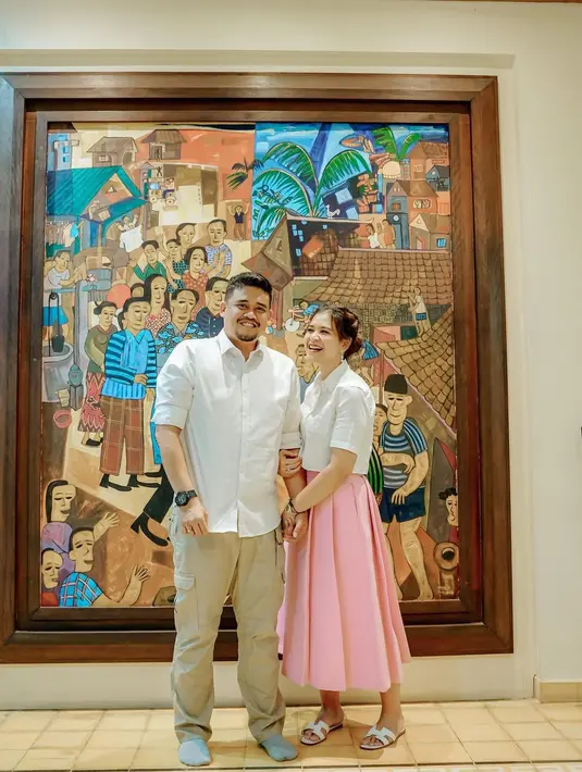 Gaya manis Kahiyang Ayu bersama sang suami. Ia mengenakan atasan kemeja lengan pendek berwarna putih, dipadu dengan midi pleated skirt pink yang serasi dan cerah. [Foto: Instagram/ayanggkahiyang]