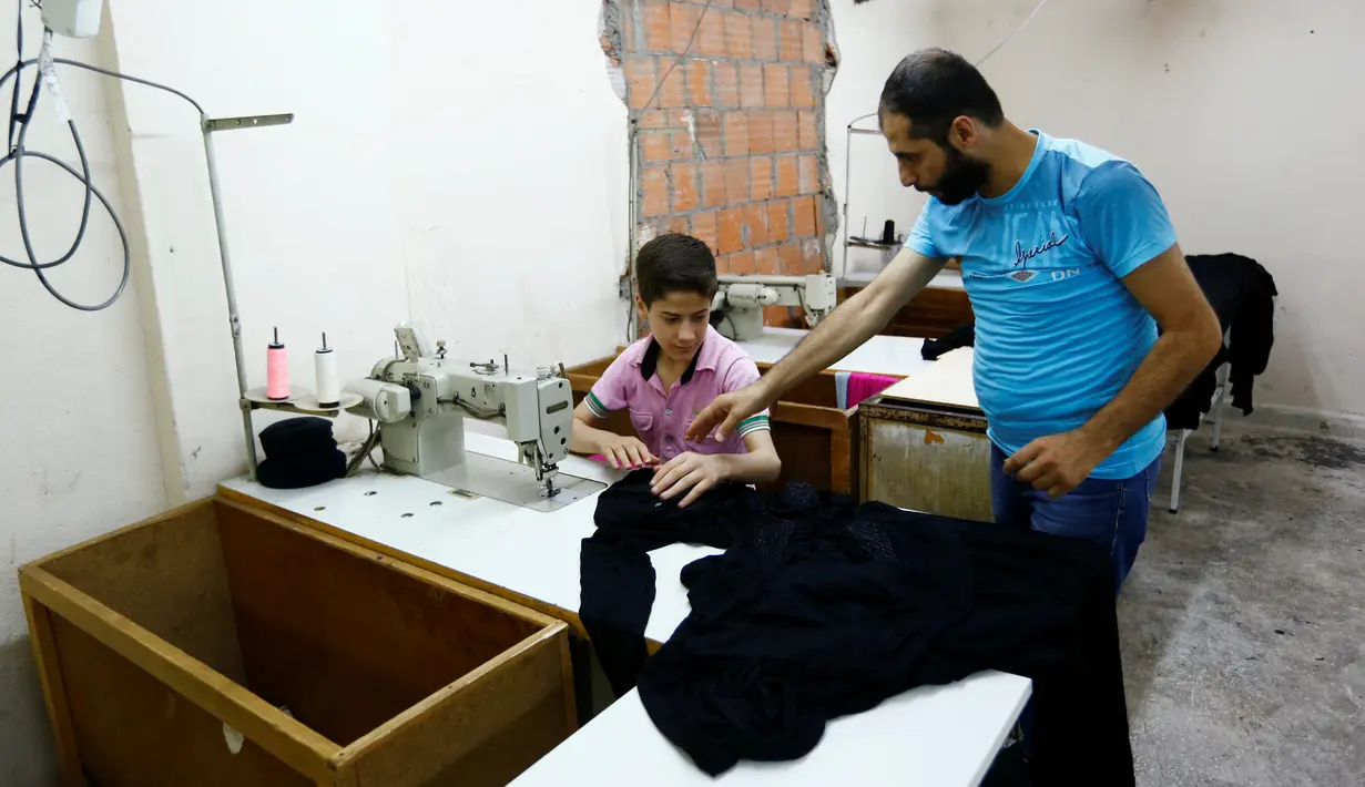  Bocah pengungsi Suriah saat mendengarkan instruksi dari ayahnya yang juga bekerja di pabrik tekstil, Istanbul, Turki, (24/6). Mereka bekerja untuk membantu orang tuanya untuk hidup selama mengungsi di Turki. (REUTERS/Umit Bektas)