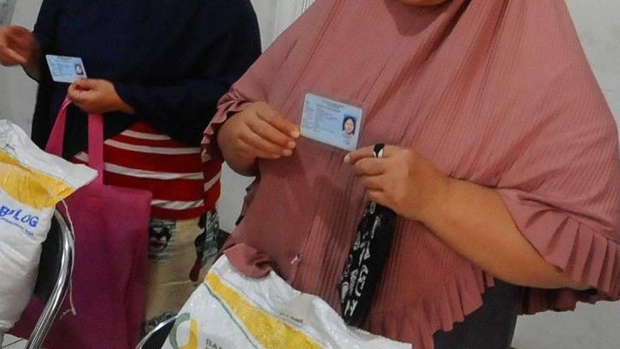 Warga memegang kartu identitas miliknya saat difoto oleh petugas usai menerima bansos beras Bulog.