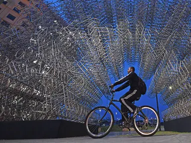 Seorang pria mengendarai sepeda melewati instalasi seni seniman China Ai Weiwei yang berjudul 'Forever Cycles' di Rio de Janeiro, Brasil, Senin (19/8/2019). Instalasi ini terdiri lebih dari 1.000 sepeda stainless steel. (CARL DE SOUZA/AFP)