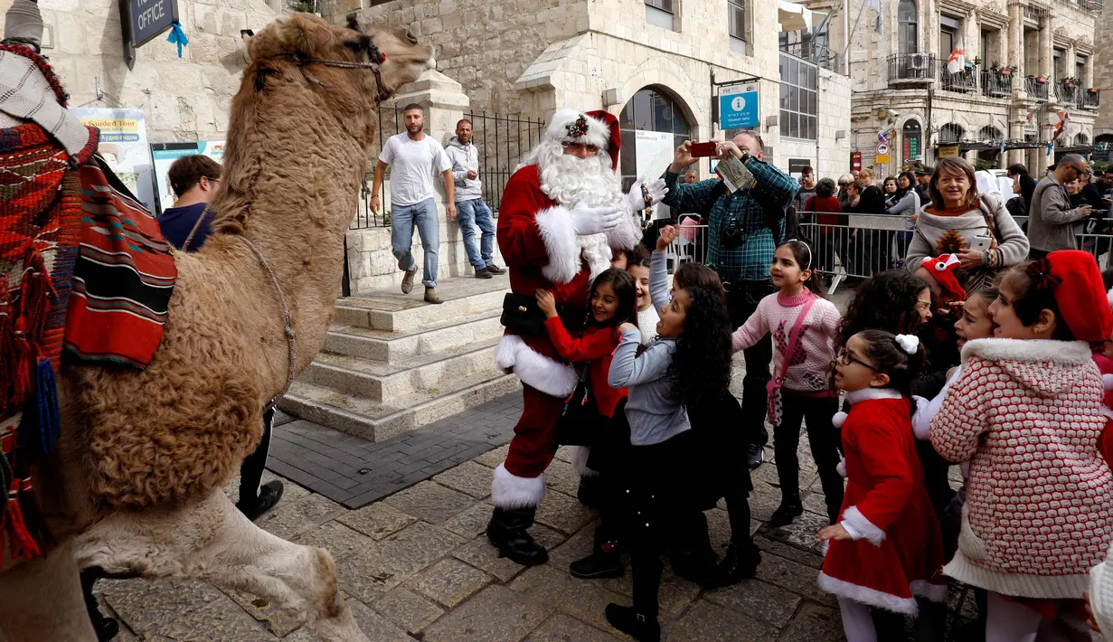 Anak-anak melihat unta yang dikendarai seorang pria mengenakan busana seperti Santa Claus di sepanjang tembok Ottoman Kota Tua Yerusalem (21/12). (AFP Photo/Gali Tibbon)