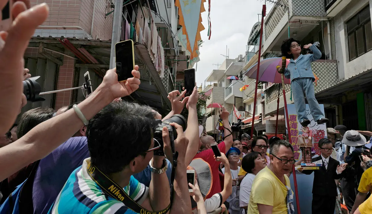 Warga mengambil gambar anak-anak yang mengenakan kostum saat perayaan Festival Cheung Chau Bun di Hong Kong (5/3). Tujuan perayaan ini agar dewa bisa menghilangkan roh jahat yang ada di pulau tersebut. (AP Photo/Vincent Yu)