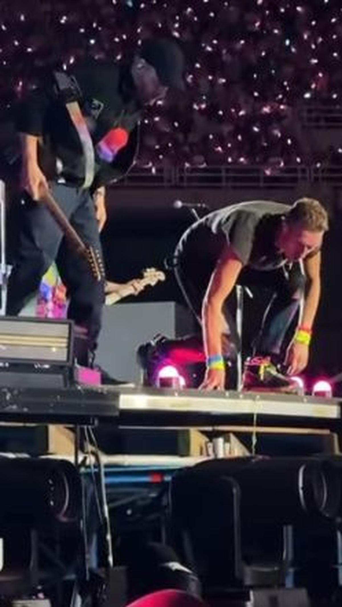 Usai menghentikan penampilan mereka, Chris Martin dan gitaris Coldplay, Johnny Buckland, melihat ke bawah dari tepi panggung untuk memastikan penonton tersebut baik-baik saja.