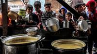 Anak-anak menunggu sambil memegang panci kosong bersama pengungsi Palestina lainnya untuk mendapatkan makanan menjelang berbuka puasa selama bulan suci Ramadhan, di Rafah di Jalur Gaza Selatan pada 16 Maret 2024. (SAID KHATIB/AFP)