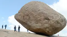Pengunjung berdiri dekat batu 'Krishna's Butter Ball' yang terkenal di Mahabalipuram, India, Kamis (3/10/2019). Batu yang dikenal masyarakat sekitar dengan nama Vaan Irai Kal ini terletak di lereng dengan kemiringan 45 derajat. (ARUN SANKAR / AFP)