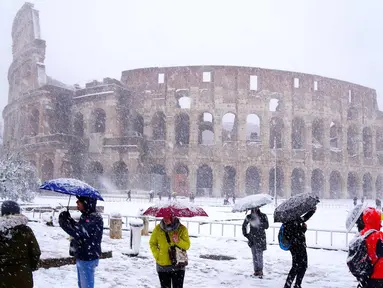 Sejumlah wisatawan mengabadikan Colosseum kuno saat hujan salju di Roma, Italia (26/2). (AFP Photo/Vicenzo Pinto)