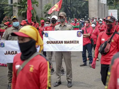 Petugas Satpol PP memegang poster imbauan protokol kesehatan COVID-19 saat unjuk rasa buruh di depan Gedung DPR, Jakarta, Selasa (17/11/2020). Pemerintah terus mengingatkan pentingnya 3M yaitu memakai masker, menjaga jarak, dan mencuci sebagai upaya pencegahan Covid-19. (Liputan6.com/Faizal Fanani)
