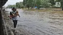 Warga melintasi banjir di Jalan Ahmad Yani, Cempaka Putih, Jakarta, Minggu (23/2/2020). Banjir yang terjadi dari dini hari tadi melumpuhkan akses jalan tersebut. (Liputan6.com/Herman Zakharia)