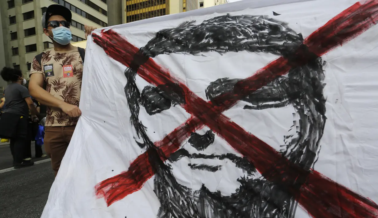 Seorang demonstran memegang spanduk dengan tanda x di atas gambar Presiden Brasil Jair Bolsonaro, di Sao Paulo, Sabtu (3/7/2021). Protes ini dipicu oleh tuduhan korupsi baru-baru ini yang melibatkan pembelian vaksin COVID-19 oleh kementerian kesehatan. (AP Photo/Nelson Antoine)