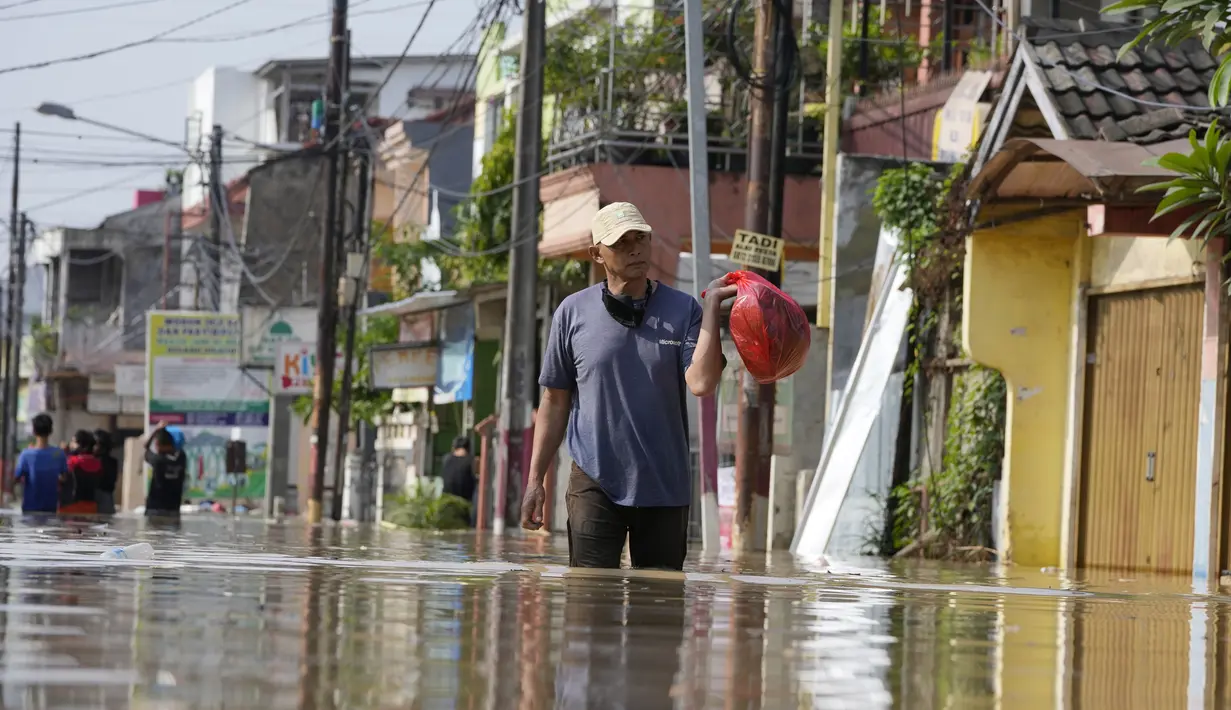 Seorang pria berjalan melalui jalan yang banjir di Bekasi, Jawa Barat, Kamis (17/2/2022). Hujan deras yang dikombinasikan dengan perencanaan pembuangan limbah kota yang buruk sering menyebabkan banjir besar. (AP Photo/Achmad Ibrahim)