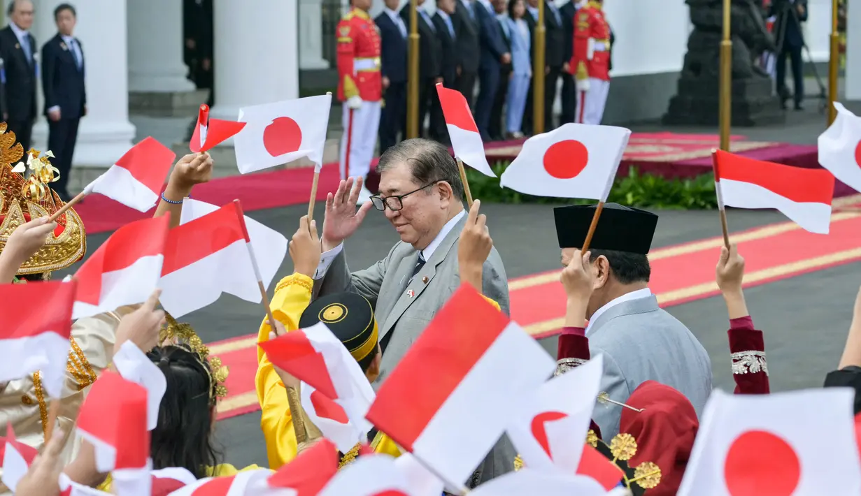 Kedatangan PM Shigeru Ishiba lalu disambut murid sekolah yang mengibarkan bendera Indonesia dan Jepang sambil mengucapkan kalimat selamat datang dalam bahasa Jepang. (Bay ISMOYO/AFP)