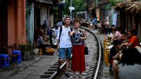 Foto pada 8 Juni 2019 memperlihatkan wisatawan berswafoto di tengah jalur kereta api populer di Hanoi. Di ibu kota Vietnam tersebut rel-rel kereta yang berada di permukiman padat penduduk dijadikan destinasi wisata selfie. (Photo by Manan VATSYAYANA / AFP)
