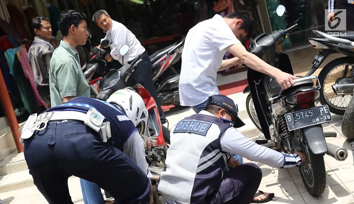 Petugas mengempeskan ban motor saat melakukan penertiban di kawasan pusat perbelanjaan Pasar Baru, Jakarta, Rabu (21/2). Penertiban dilakukan dengan membongkar lapak PKL serta kendaraan yang parkir di trotoar. (Liputan6.com/Immanuel Antonius)