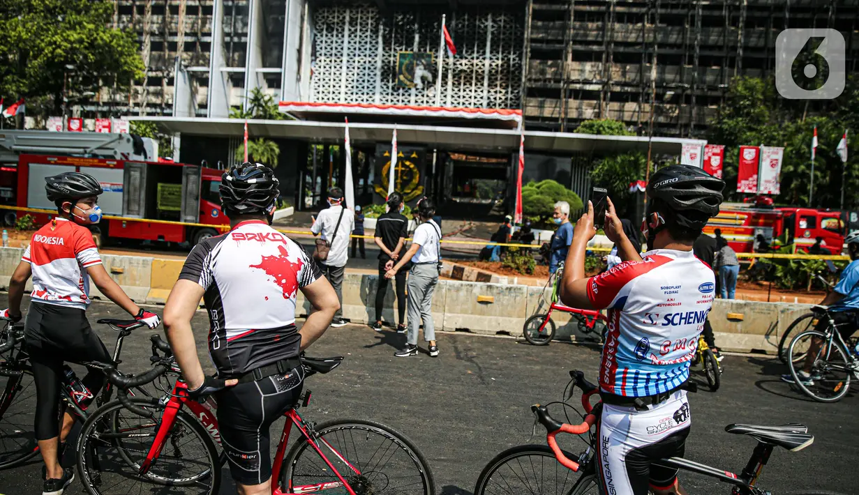Sejumlah pesepeda mengambil gambar gedung utama Kejaksaan Agung RI yang terbakar di Jalan Sultan Hasanuddin, Jakarta Selatan, Minggu (23/8/2020).  Banyak warga yang memadati Jalan Hasanuddin untuk melihat langsung kondisi gedung Kejaksaan Agung yang hangus dilalap api. (Liputan6.com/Faizal Fanani)