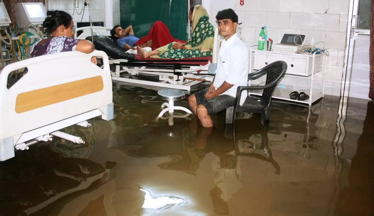 Pasien dan anggota keluarganya berada di dalam bangsal yang tergenang banjir di Nalanda Medical College Hospital, daerah Bihar, India, 29 Juli 2018. Rumah sakit itu digenangi air kotor dengan sejumlah ikan terlihat berenang memenuhi lantai. (AFP PHOTO)
