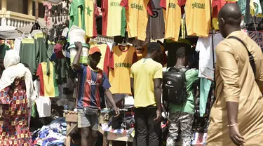 Seorang pria berjalan melewati kios yang menjual kaus tim sepak bola Senegal di Dakar (4/2/2022). Senegal akan bertanding melawan Mesir pada babak final Piala Afrika 2021 di Paul Biya stadium, Senin (7/2/2022) dini hari WIB besok. (AFP/Seyllou)