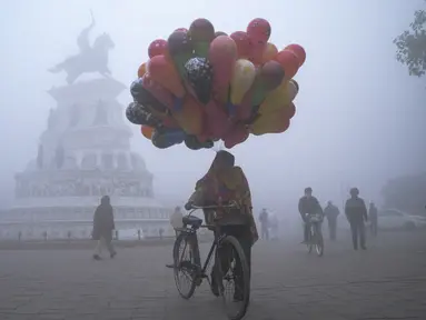 Seorang penjual balon berjalan di sepanjang jalan Heritage di tengah kabut tebal di hari yang dingin di Hari Tahun Baru, di Amritsar (1/1/2021). Gelombang Dingin, Kabut Tebal Mencengkeram India Utara di Hari Tahun Baru di Delhi. (AFP/Narinder Nanu)