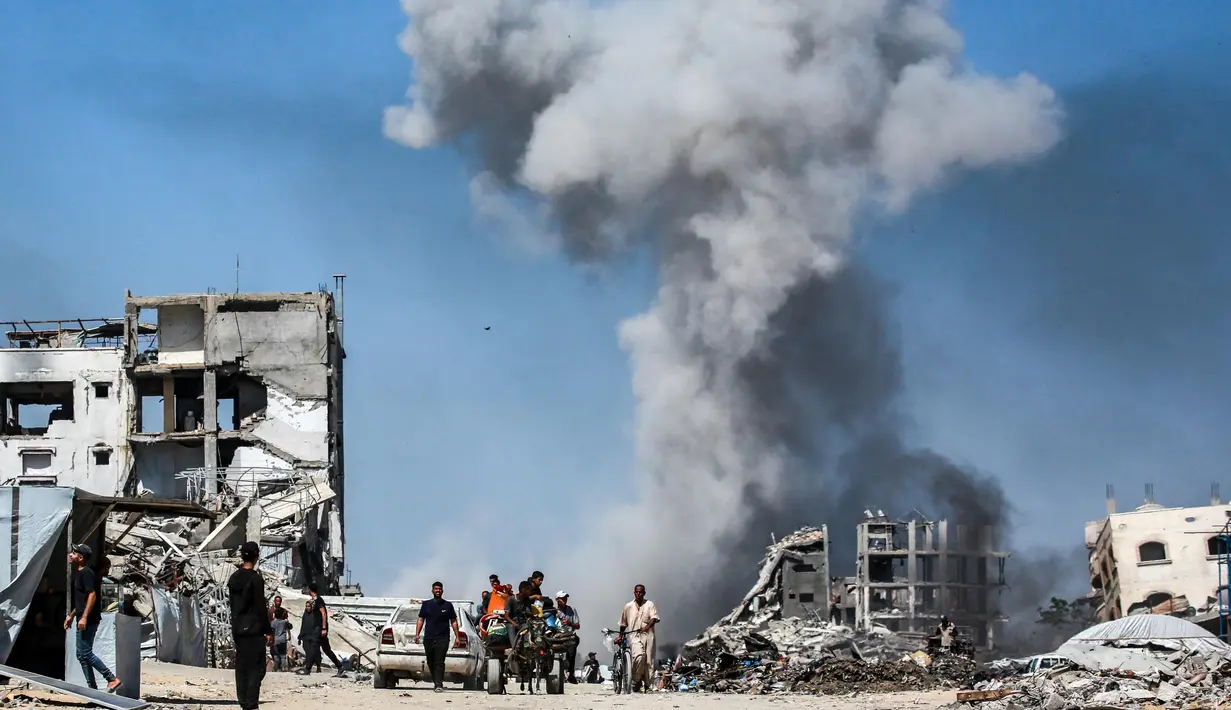 Orang-orang bergerak melewati bangunan yang hancur berlatar belakang kepulan asap menyusul serangan Israel di Jabalia, Jalur Gaza utara pada 25 Mei 2025. (Bashar TALEB/AFP)
