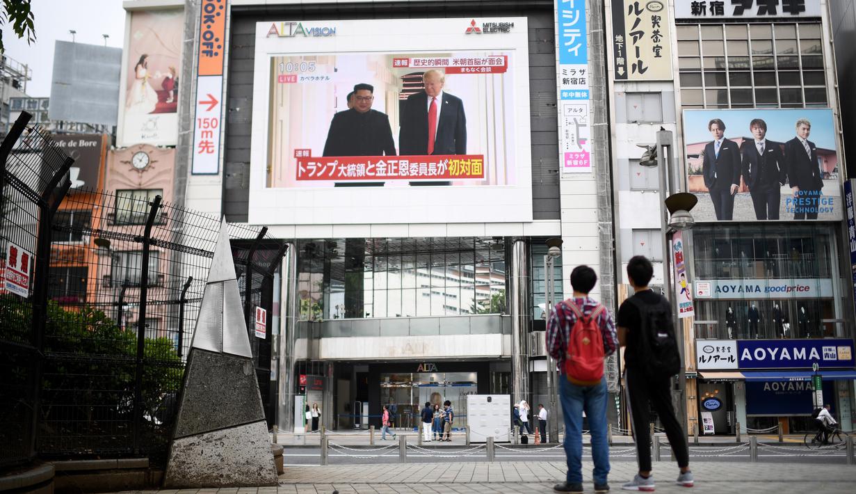 Pejalan kaki melihat layar yang menampilkan pertemuan antara pemimpin Korea Utara Kim Jong-un dan Presiden AS Donald Trump di Tokyo, Selasa (12/6). Untuk pertama kalinya dalam sejarah, Donald Trump dan Kim Jong-un bertemu. (AFP PHOTO/Martin BUREAU)