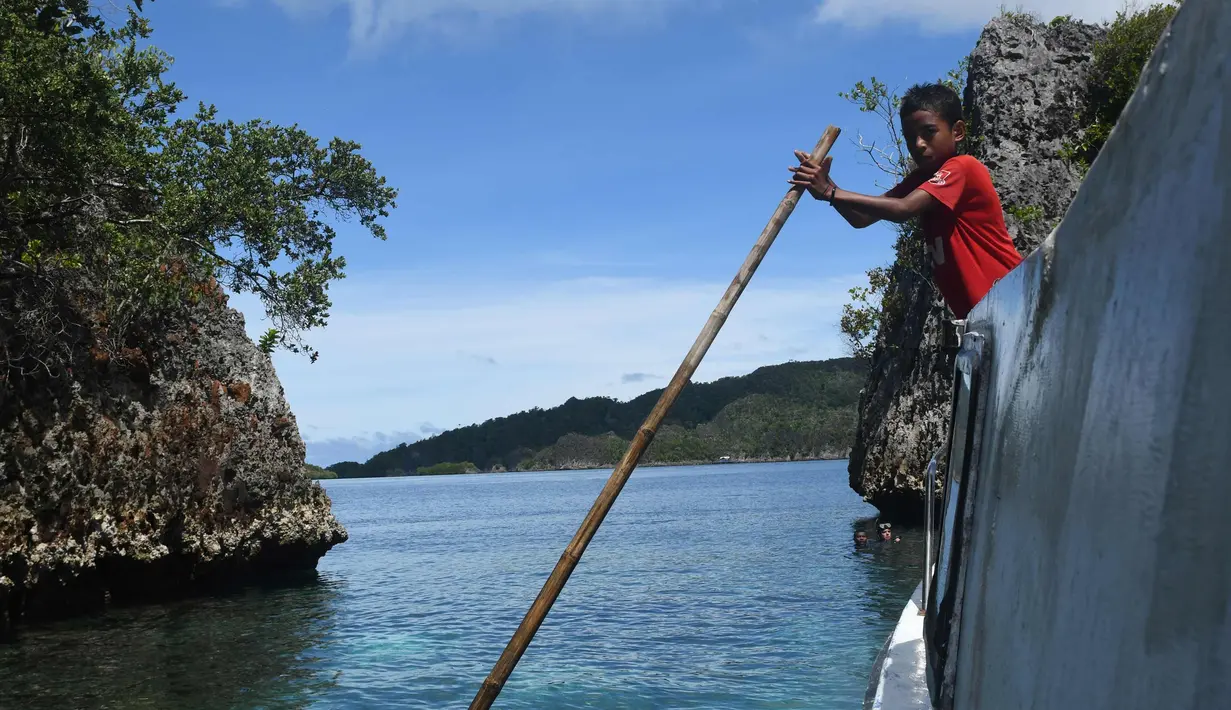 Seorang anak laki-laki dari suku Byak Betew membantu menggerakkan kapal untuk membawa pengunjung ke pulau Raja Ampat 20 Agustus 2017. Raja Ampat merupakan rumah bagi sekitar 1.400 jenis ikan dan 600 spesies karang. (AFP Photo/Goh Chai Hin)