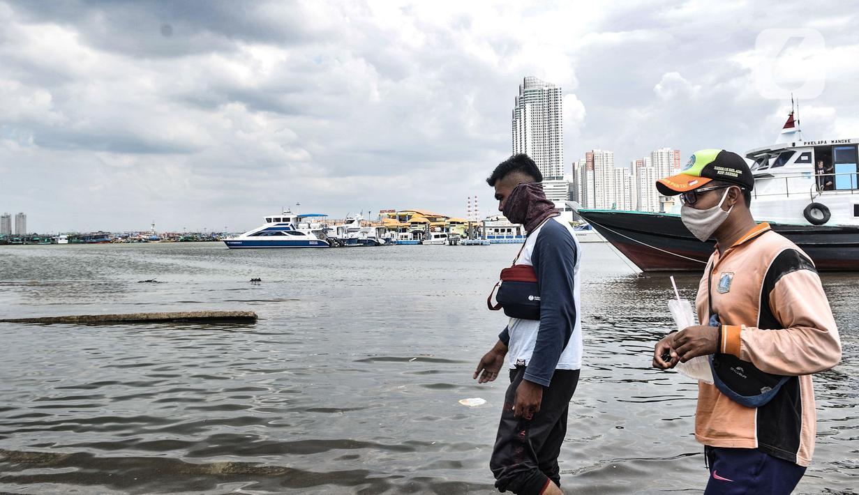 Petugas melintasi kapal yang tidak beroperasi saat banjir rob merendam Pelabuhan Kali Adem, Muara Angke, Jakarta, Kamis (22/10/2020). Banjir akibat air pasang dengan ketinggian mencapai 30 cm tersebut telah merendam kawasan Pelabuhan Kali Adem dan sudah berlangsung selama lima hari. (merdeka.com/Iqb
