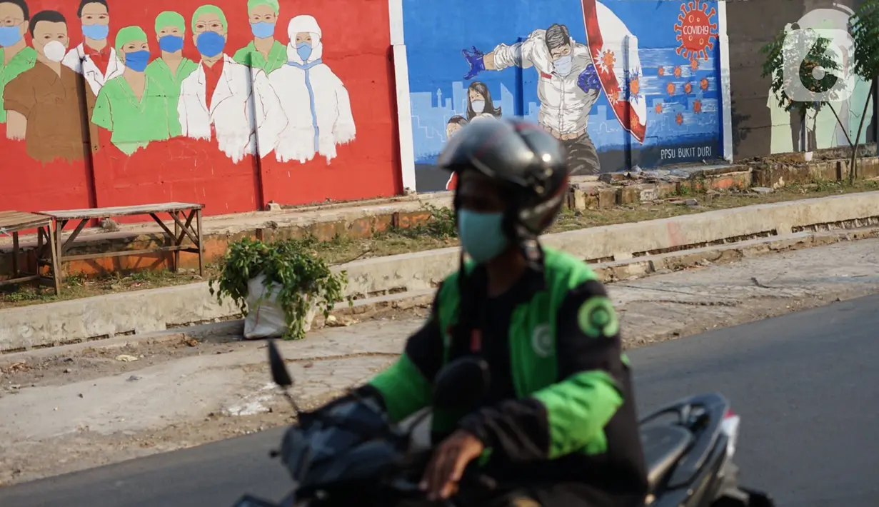 Pengendara motor melintas di depan mural bertema covid-19 di Bukit Duri, Jakarta, Minggu (30/8/2020). Mural yang dibuat petugas PPSU bertujuan mengingatkan masyarakat akan bahaya covid-19, sehubungan dengan masih tingginya jumlah kasus positif covid-19 di Jakarta. (Liputan6.com/Immanuel Antonius)