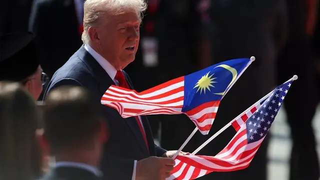 Presiden Donald Trump mengangkat bendera Malaysia dan Amerika Serikat dalam upacara penyambutan setibanya di Bandara Internasional Kuala Lumpur, Minggu (26/10/2025) untuk menghadiri KTT ke-47 ASEAN.