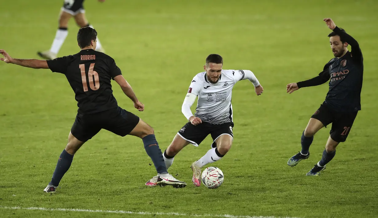 Gelandang Swansea City, Matt Grimes (tengah) berusaha melewati dua pemain Manchester City Rodri dan Bernardo Silva pada laga perdelapan final Piala FA di di Liberty Stadium di Swansea, Wales, Kamis (11/2/2021). Kemenangan ini membuat City lolos ke perempat final Piala FA. (Nick Potts/PA via AP)
