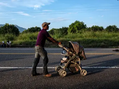 Seorang imigran Honduras mendorong kereta bayi dalam perjalanannya menuju Amerika Serikat di negara bagian Oaxaca, Meksiko, 29 Oktober 2018. Kereta dorong bayi telah menjadi barang mewah bagi para imigran dalam perjalanan mereka. (Guillermo Arias/AFP)