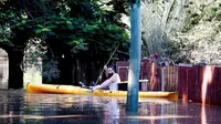 Seorang pria mengirimkan pasokan kepada penduduk yang terdampar di Fairfield di Brisbane, Australia akibat banjir, Selasa, 1 Maret 2022. (AP Photo/Tertius Pickard)