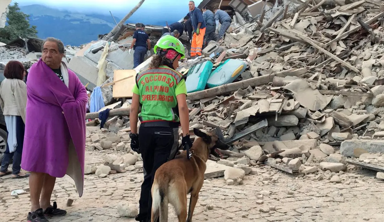Seorang pria dan petugas penyelamat serta anjing pelacak berdiri di depan puing bangunan rumah yang rusak akibat gempa  6,2 SR di Amatrice, Italia tengah, Kamis (24/8). Sedikitnya enam orang tewas dalam bencana ini. (REUTERS/Emiliano Grillotti)