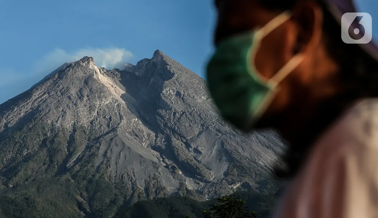 Seorang pria melintas dengan latar belakang aktivitas gunung merapi terlihat dari Lapangan Stiper, Glagaharjo, Cangkringan, Sleman, Kamis (19/11/2020). Status Gunung Merapi sudah dinaikkan pada 5 November 2020 lalu dari waspada level II menjadi siaga level III. (Liputan6.com/Johan Tallo)
