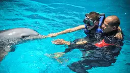 Pelatih lumba-lumba, Adrian Calderon membantu Javier Gonzalez menyentuh lumba-lumba selama sesi terapi di National Aquarium, Kuba, Senin (26/5/14). (AFP PHOTO/Adalberto ROQUE)