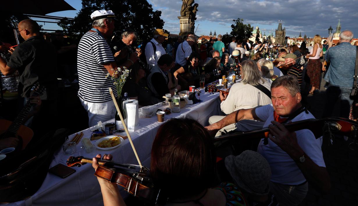 Warga memainkan musik saat makan malam bersama di atas meja sepanjang 500 meter di Charles Bridge di Praha, Republik Ceko, Selasa (30/6/2020). Kegiatan itu merupakan perpisahan simbolis yang digelar untuk menandai akhir dari masa krisis virus corona Covid-19 di negara tersebut. (AP/Petr David Josek)
