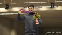 Selebrasi petembak Indonesia, Muhammad Sejahtera Dwi Putra dengan medali emas di atas podium usai memenangi lomba nomor perorangan 10 meter running target putra cabang menembak Asian Games Hangzhou 2022 di Fuyang Yinhu Sports Centre, Hangzhou, China, Senin (25/9/2023). (NOC Indonesia)