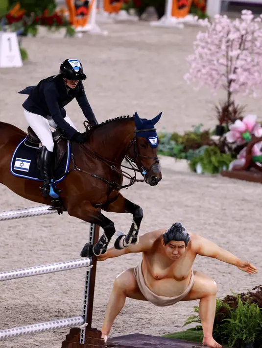 Atlet Israel Ashlee Bond menunggangi Donatello 141 melompati patung sumo (kanan) di final lompat individu berkuda selama Olimpiade Tokyo 2020 di Equestrian Park di Tokyo (4/8/2021). Beberapa atlet berkuda mengaku, kalau kuda mereka ketakutan karena adanya patung pesumo tersebut. (AFP/Behrouz Mehri)